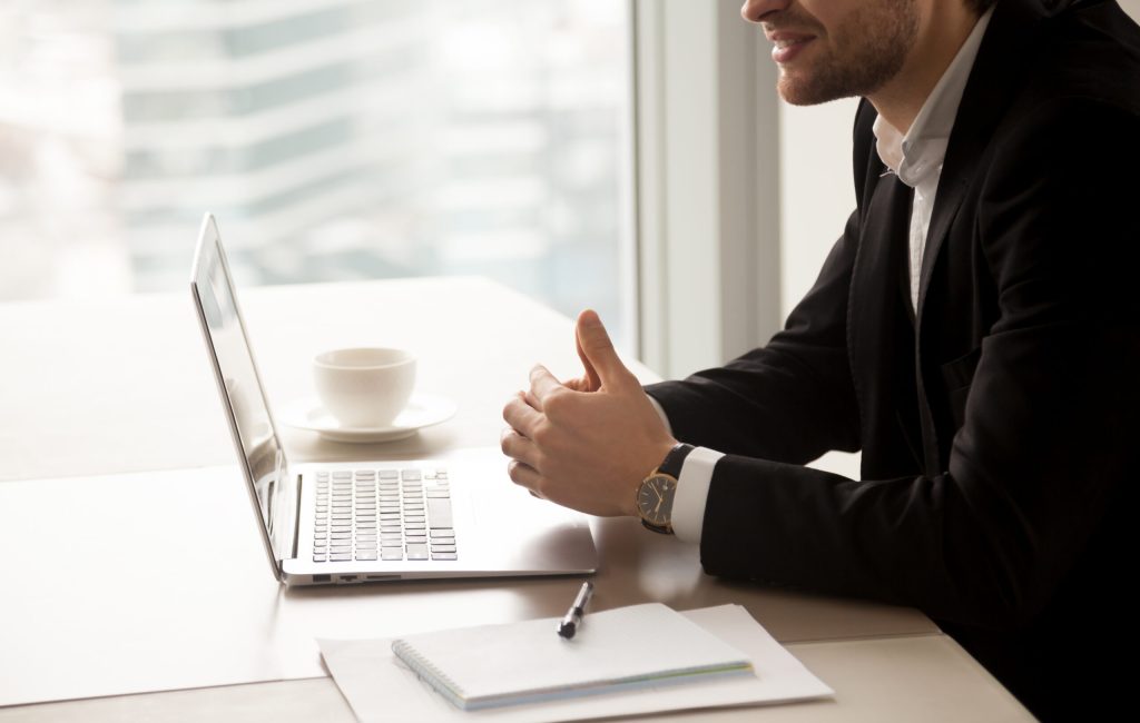 Close up photo of successful businessman sitting at desk with laptop and conducts negotiations. Male entrepreneur communicate with partners in office. Financial consulting, small business assistance